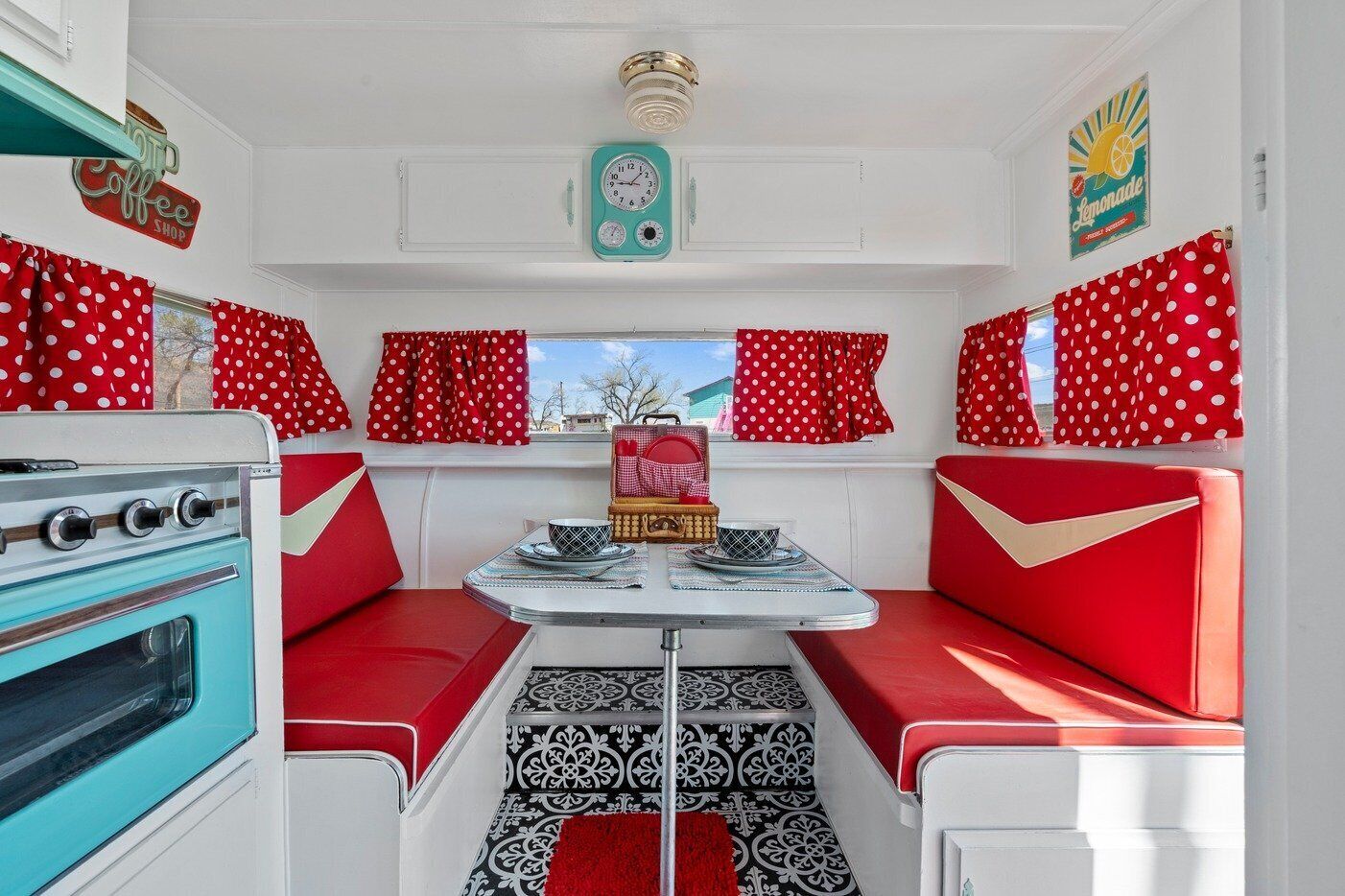 Interior compacto de autocaravana con kitchenette, una mesa de comedor y cortinas rojas con lunares.
