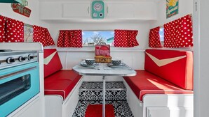 Interior d'una caravana compacta amb una cuineta, una taula de dinar i cortines amb punts vermells.