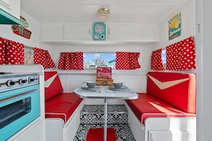 Ein kompaktes Wohnmobil-Interieur mit einer Küchenzeile, einem Esstisch und roten Punktenmuster-Vorhängen.