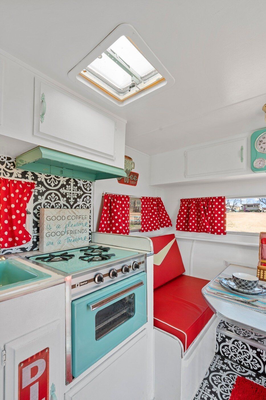 Una cocina compacta con estufa, pileta y ventana con cortinas rojas.