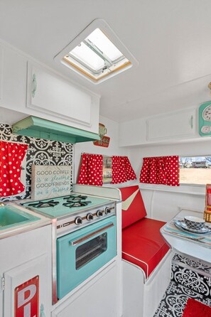 Een kleine keuken met een fornuis, een spoelbak en een raam met rode gordijnen.