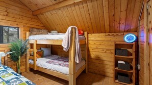 A wooden cabin room with bunk beds, a small plant, a clock, and a shelf with storage boxes. - Cadillac Cottage Retreat | 1 Unit | Near Cañon City Center (Canon City)