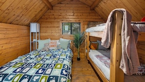 A cozy cabin with a wooden interior, a bunk bed, a bed with a patterned quilt, a small plant, and a window with a view. - Cadillac Cottage Retreat | 1 Unit | Near Cañon City Center (Canon City)