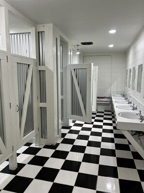Des toilettes publiques avec un sol à carreaux noirs et blancs, des murs blancs et plusieurs lavabos.
