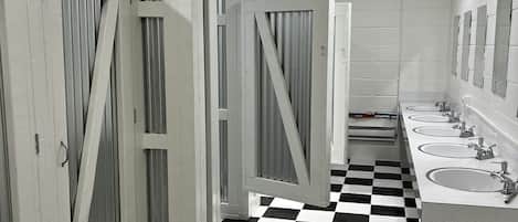 Un baño público con suelo a cuadros blancos y negros, paredes blancas y varios lavamanos.