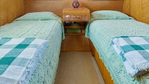 Ein kleines Zimmer mit zwei Betten, einem kleinen Nachttisch aus Holz, einer dekorativen Vase und einem Fenster mit Jalousien.