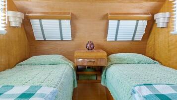 A compact room with two beds, a small wooden nightstand, a decorative vase, and a window with blinds.