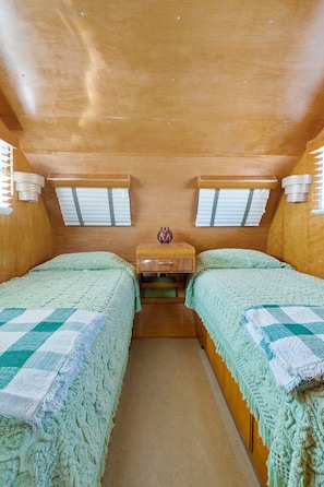 Habitación compacta con dos camas, una mesita de noche de madera, un florero decorativo y una ventana con persianas.