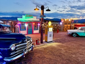 Un área con temática vintage que incluye un letrero de neón para 'Starlite Vintage Resort', una bomba de gasolina antigua y coches clásicos.