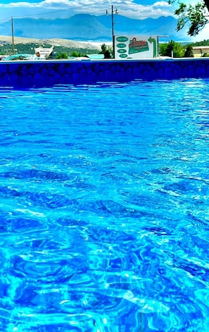 En swimmingpool med kristallklart blått vatten, omgiven av en stenmur och med utsikt över avlägsna berg.