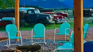 Sitzgelegenheiten im Freien mit Stühlen und einer Feuerstelle, Lichterketten über Kopf und Oldtimer im Hintergrund.