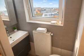 A bathroom with a window, a sink, a mirror, a radiator, and a towel rack. - Bruges by the Beach (Blankenberge)