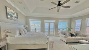 A bedroom with a bed, a nightstand, a glass-top desk, a sofa, and a ceiling fan.
