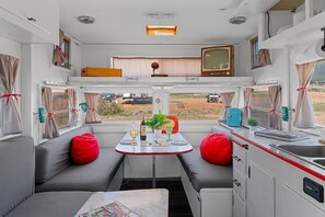 A compact RV interior with a kitchenette, seating area, and a television. - Unique Vintage Motorhome Stay | Cañon City Retreat (Canon City)