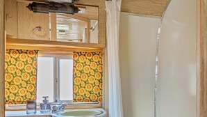 Ein kleines Badezimmer in einem Wohnmobil, mit Waschbecken, Spiegel und Dusche.