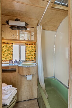 A compact RV bathroom with a sink, mirror, and shower. - Vintage Motorhome Stay | 1 Unit | Cañon City, CO (Canon City)