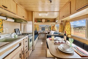 A compact RV kitchen with a dining area, a stove, sink, and a window with a view of the outdoors.