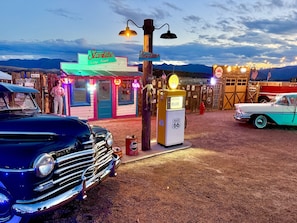 Un área con temática vintage que incluye un letrero de neón para 'Starlite Vintage Resort', una bomba de gasolina antigua y coches clásicos.