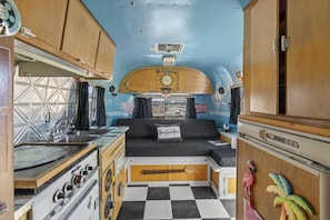 Interior compacto de autocaravana con kitchenette, cama y baño pequeño.