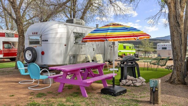 Ein Wohnmobil mit Picknicktisch und Stühlen, einem Grill und einem bunten Sonnenschirm.