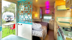 Interior compacto de una autocaravana con cama, kitchenette y zona de comedor.