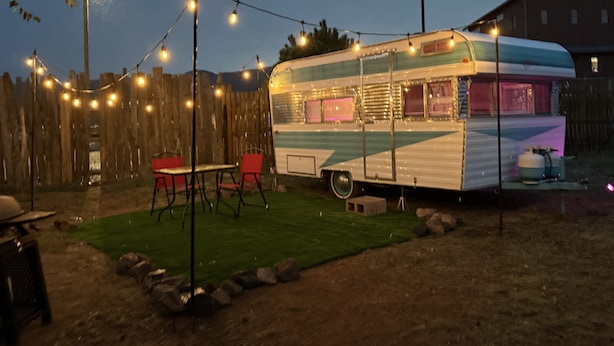 Una caravana estacionada con área de cocina, patio cercado y luces colgantes.