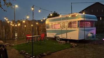 A stationary RV with a kitchen area, a fenced yard, and string lights.