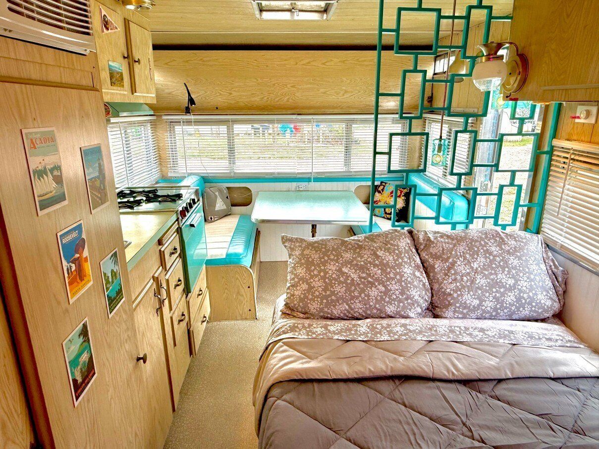 A compact RV interior with a kitchenette, a bed, and a dining area.