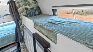 A compact RV interior with a bunk bed, a small window, and a view of the outside. - Vintage Motorhome Stay | Unique Experience | Cañon City, CO (Canon City)