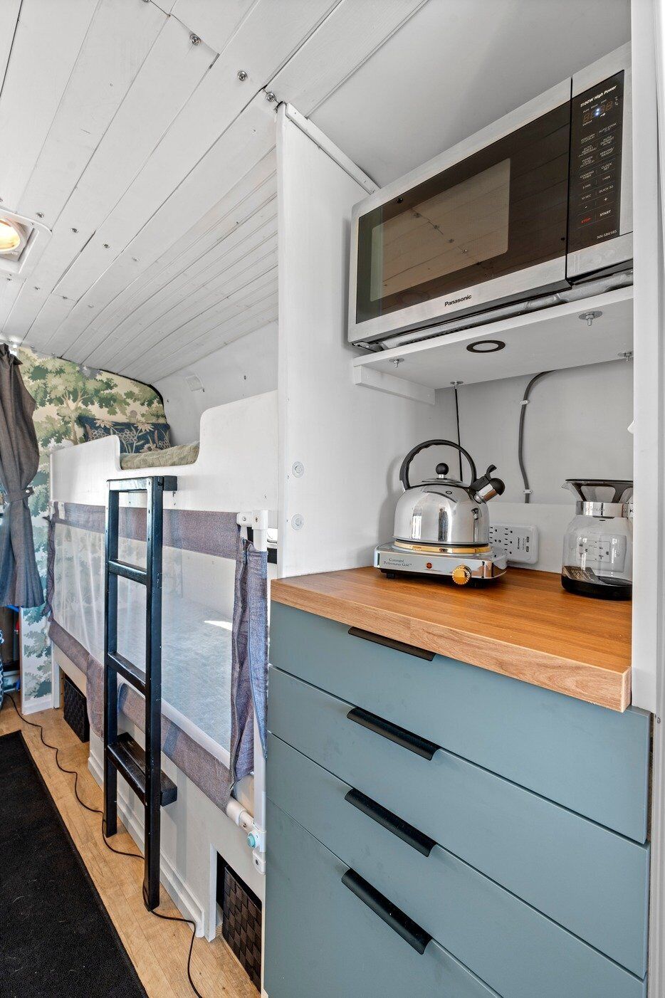 A compact kitchenette with a microwave, kettle, and coffee maker on a wooden countertop.