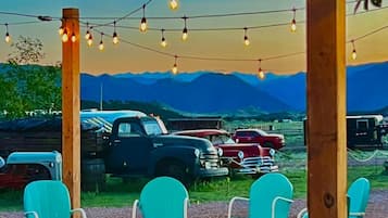 Outdoor seating with chairs and a fire pit, string lights overhead, and vintage cars in the background.