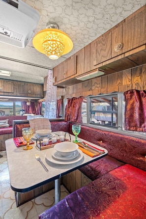 A compact RV interior with a dining area, seating, and a window providing a view. - Vintage Resort Stay | Magic Lamp | Cañon City, CO (Canon City)
