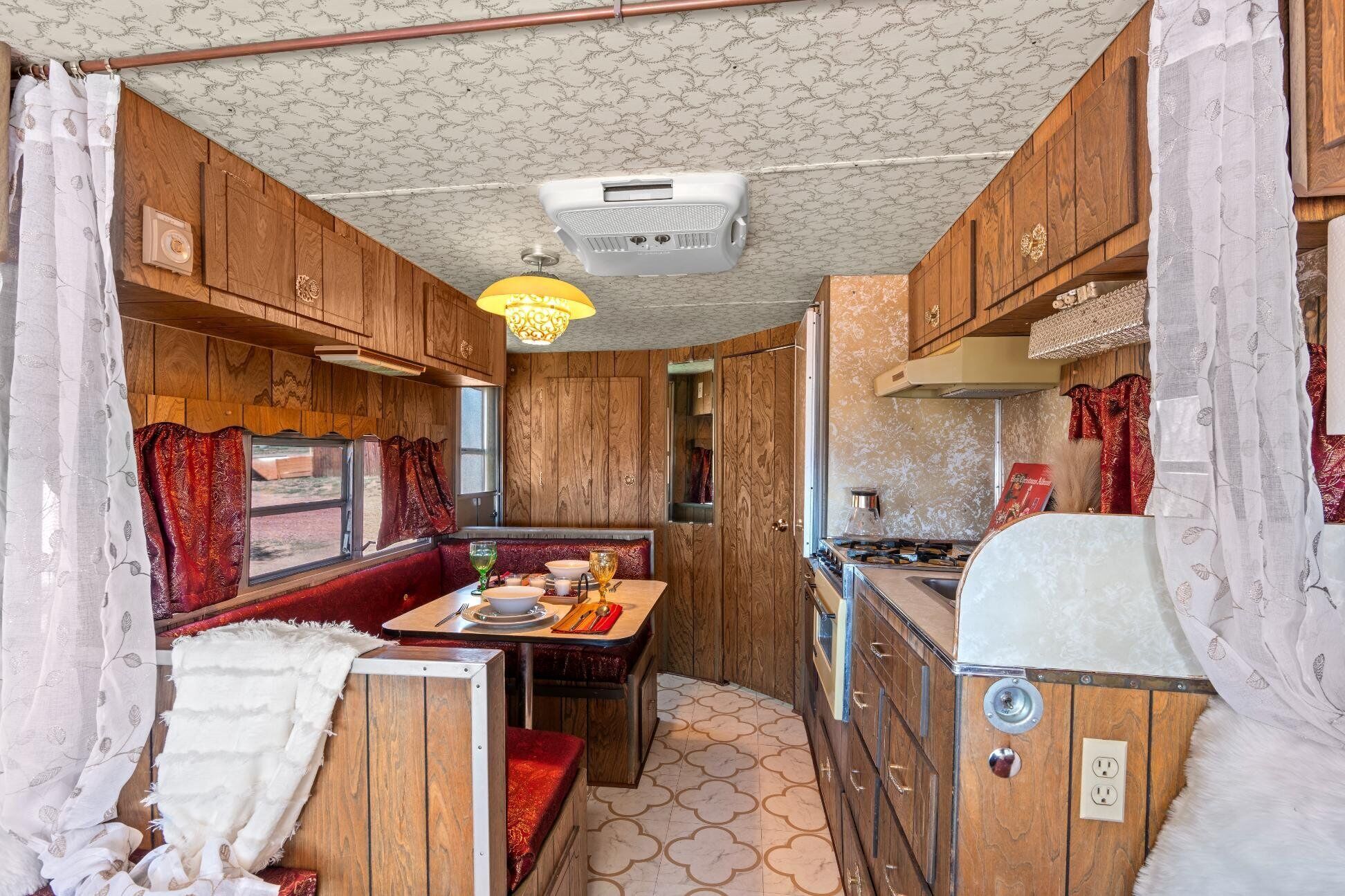 A compact RV interior with a dining area, kitchenette, and a ceiling fan.