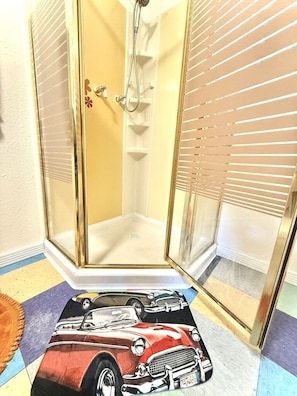 A shower with a glass door, a showerhead, and a tiled floor with a vintage car design. - Vintage Retro Apartment | Modern Comfort | Cañon City Center (Canon City)