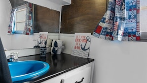 A compact kitchen with a blue sink, white cabinets, and a window with patterned curtains. - Vintage Motorhome Retreat | Unique Stay in Cañon City (Canon City)