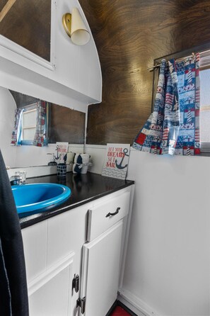 Una cuina compacta amb un rentaplat blau, armaris blancs i una finestra amb cortines estampades.