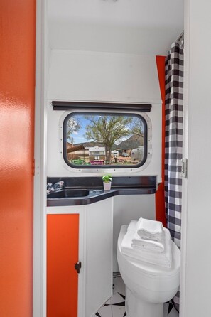 A compact bathroom with a window, a toilet, and a sink. - Vintage Motorhome Stay | Unique Orange Beauty | Cañon City (Canon City)
