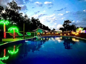 A swimming pool with a slide and neon palm tree decorations. - Vintage Motorhome Stay | Unique Orange Beauty | Cañon City (Canon City)