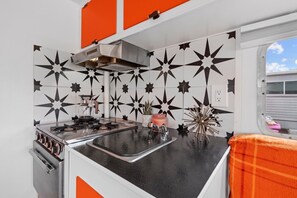 Une cuisine de taille réduite, équipée d’une cuisinière, d’un évier et d’une fenêtre donnant sur un paysage agréable.