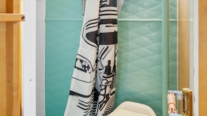 Ein Badezimmer mit Toilette, einer Duschvorhang mit grafischem Muster und einer grünen Fliesenwand.
