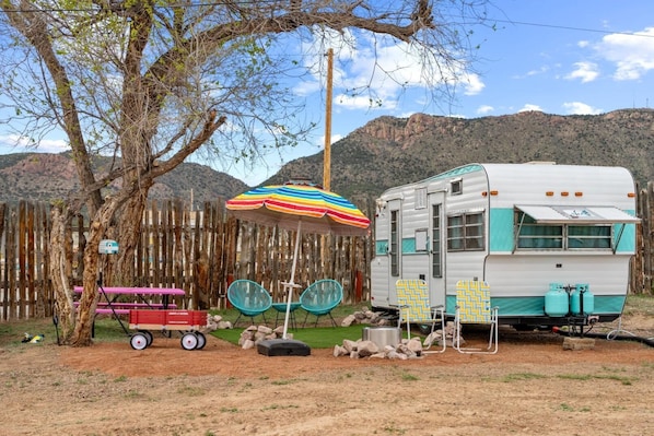 Una autocaravana antigua con un toldo turquesa, una valla de madera y un árbol al fondo.
