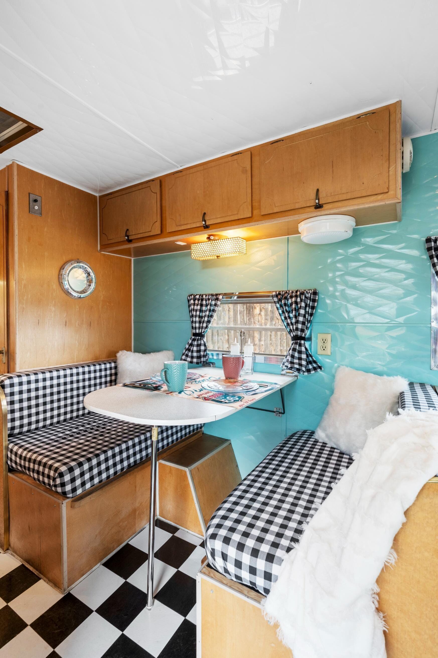 A compact kitchenette with wooden cabinets, a small table, and checkered seating.
