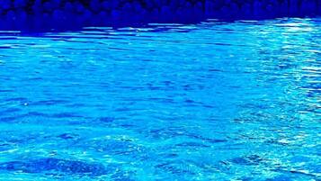 A swimming pool with clear blue water, surrounded by a stone wall and a view of distant mountains.