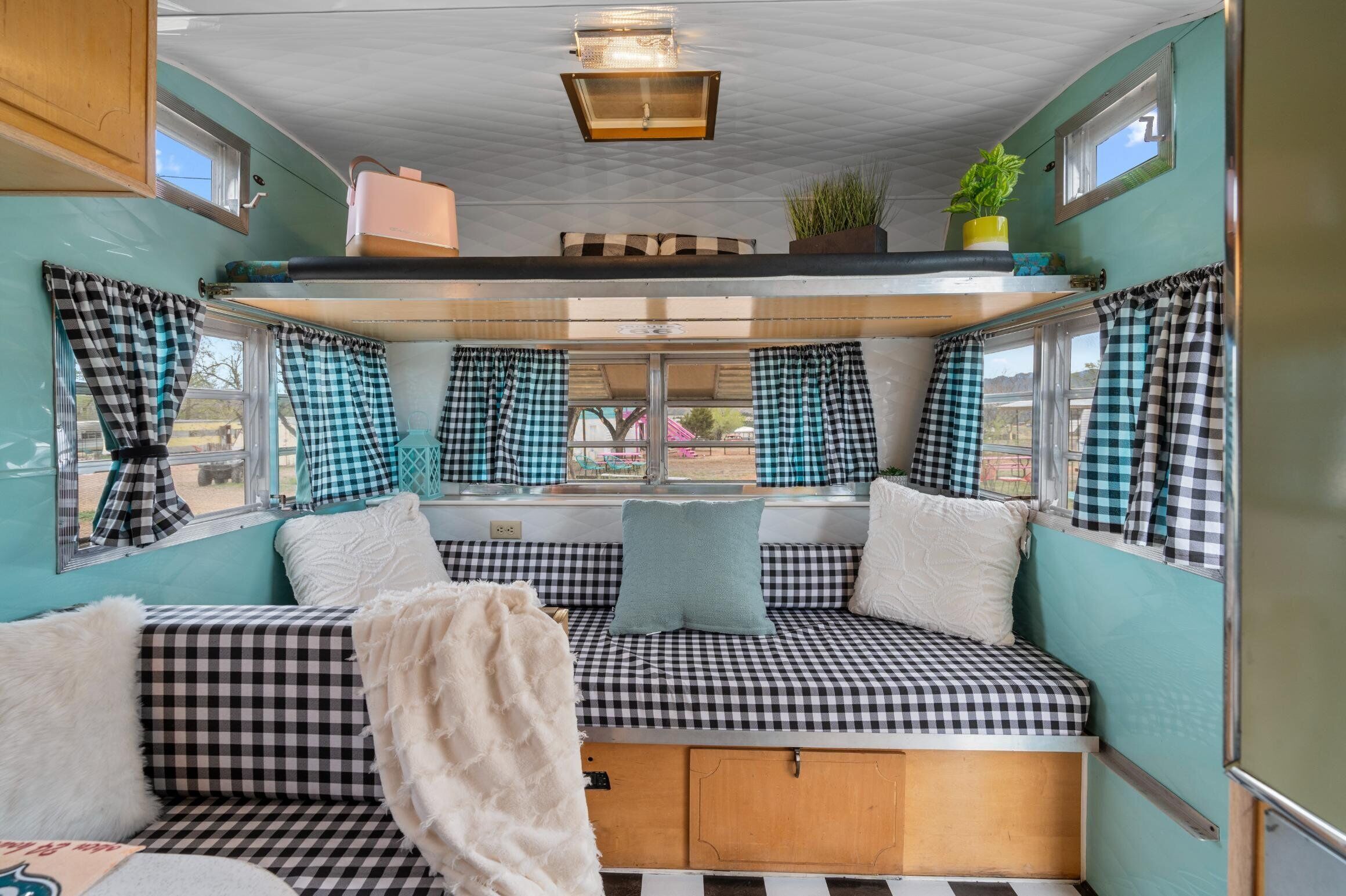 A cozy interior with checkered seating, a window with curtains, a ceiling light, and a small plant.