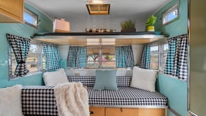 Ein gemütliches Interieur mit karierten Sitzgelegenheiten, einem fenster mit Vorhängen, einer Deckenleuchte und einer kleinen Pflanze.