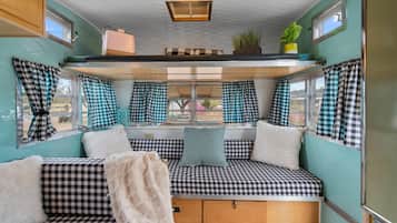 A cozy interior with checkered seating, a window with curtains, a ceiling light, and a small plant.