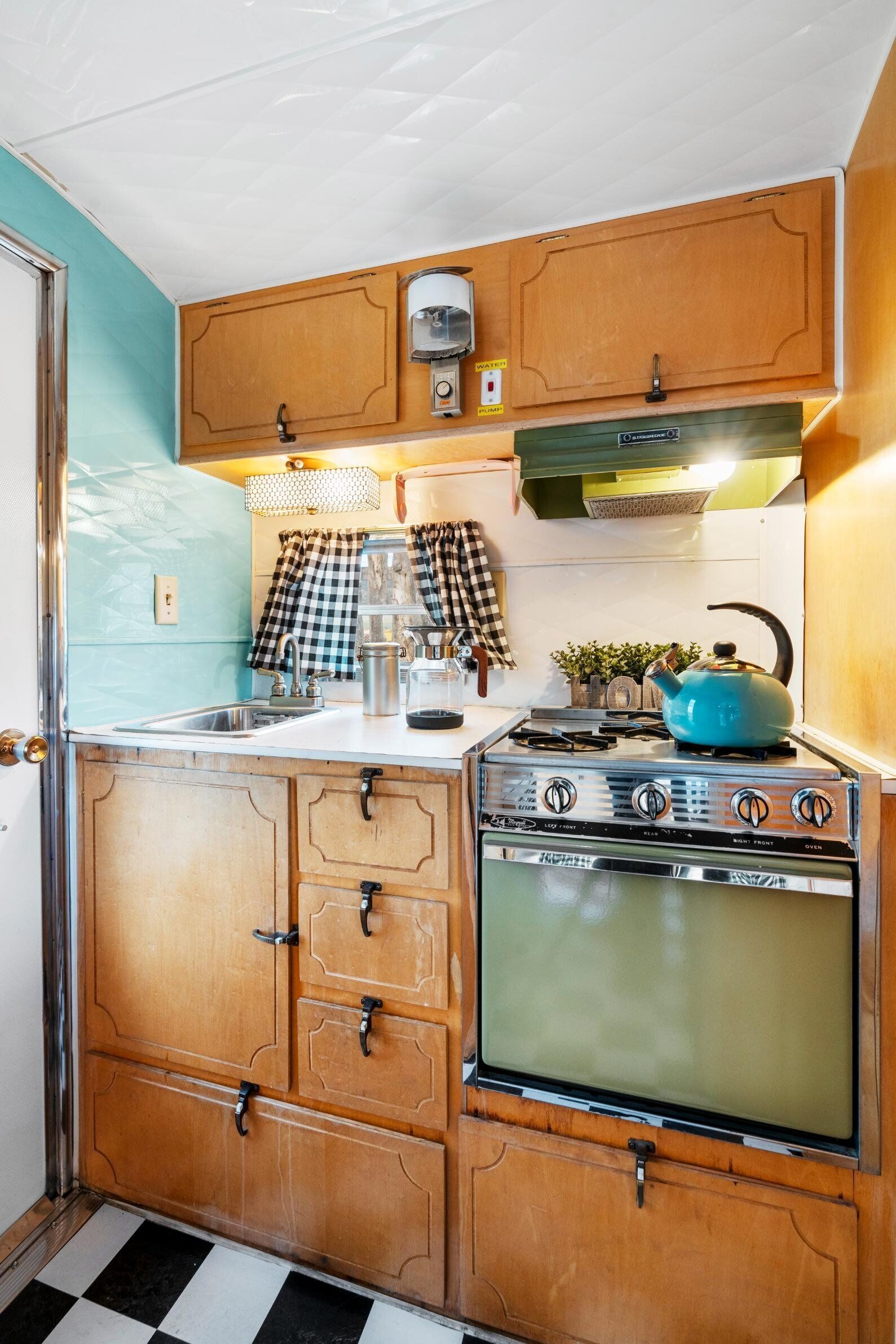 A compact kitchen with wooden cabinets, a stove, a sink, and a checkered curtain.