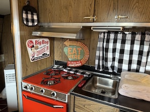 A compact kitchen with a red stove, a sink, and wooden cabinetry. - Vintage Trailer Stay | 1 Unit | Near Ruby's Diner in Cañon City (Canon City)