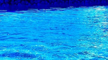 A swimming pool with clear blue water, surrounded by a stone wall and a view of distant mountains.