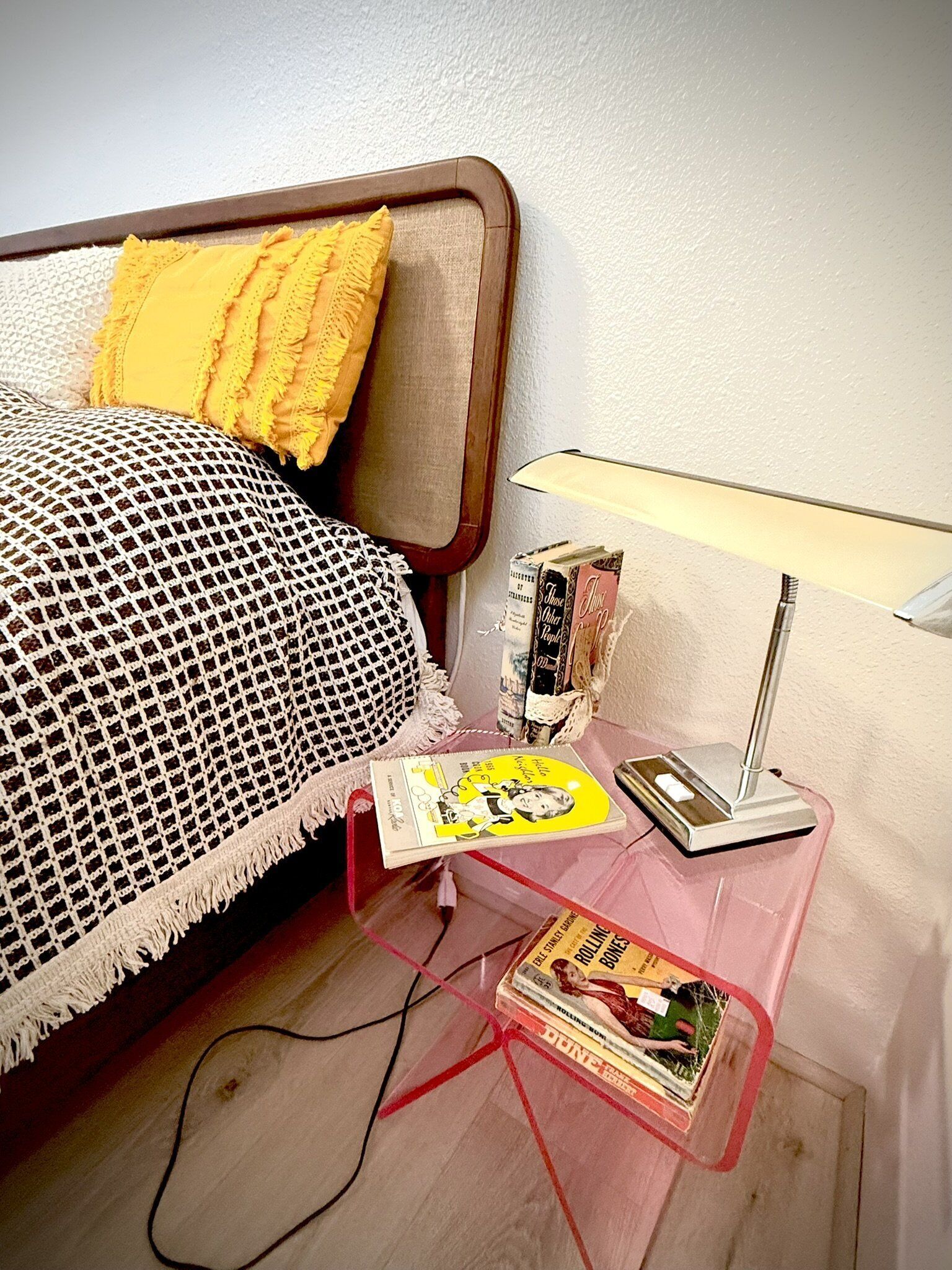 Ein ordentlich eingerichtetes Schlafzimmer mit einem Bett, einem Nachttisch mit Büchern, einer Lampe und einem kleinen Tisch mit einer Zeitschrift.